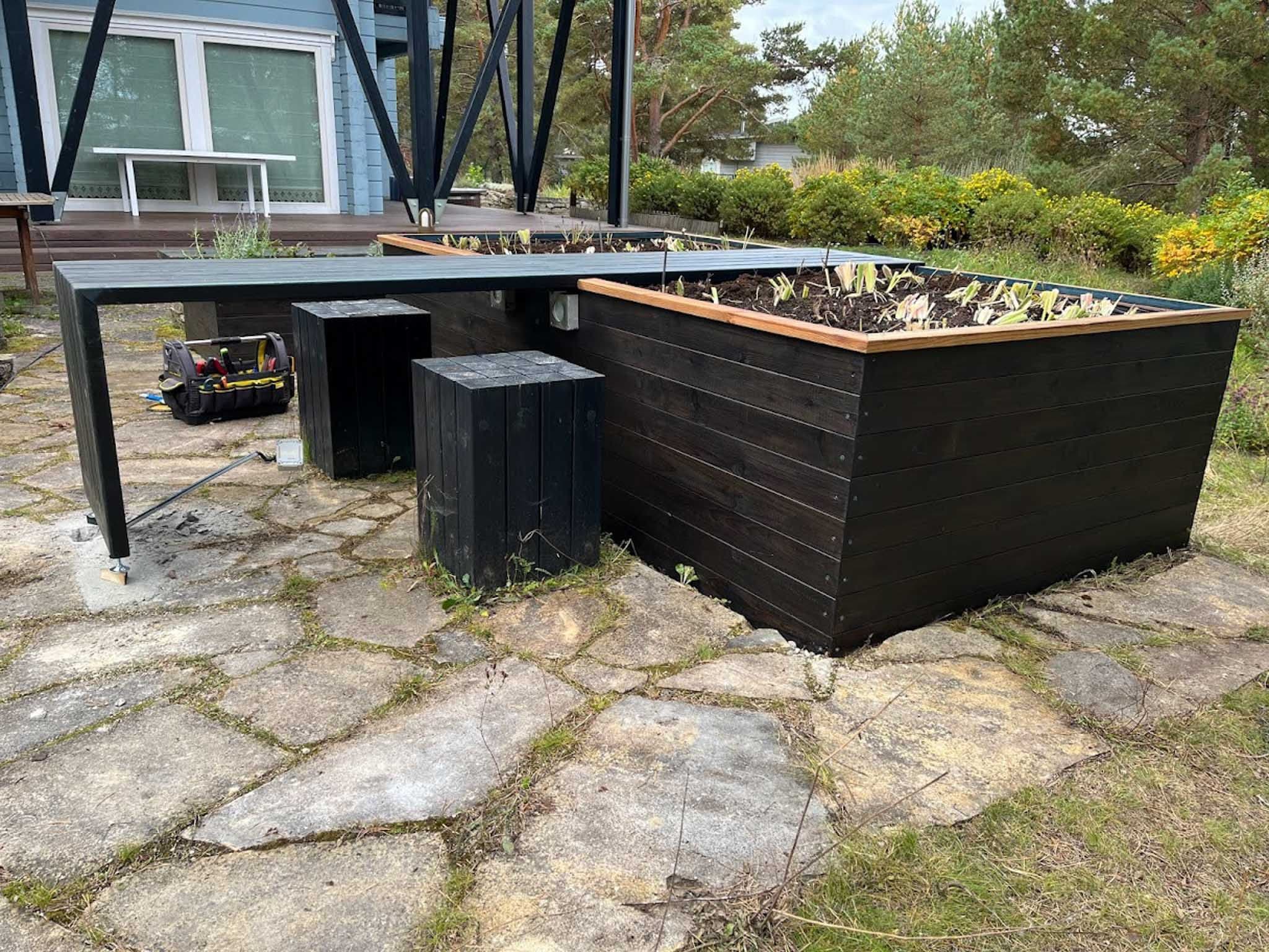 Mustaks viimistletud eritellimusel valmistatud peenrakastid koos integreeritud puidust istumisala ja lauaga.